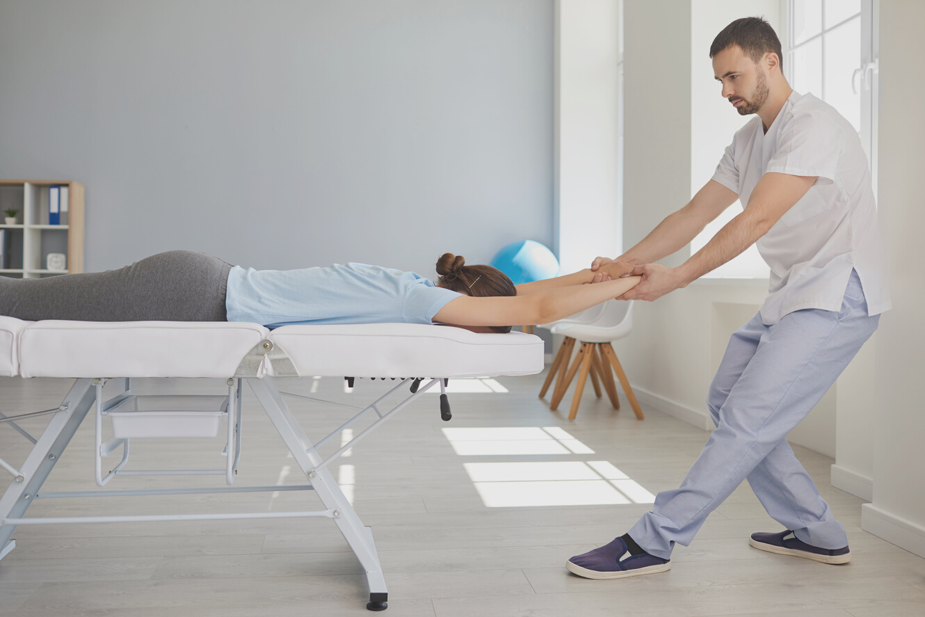 Man Chiropractor or Osteopath Stretching Woman Patients Arms and Back during Visit in Manual Therapy Clinic